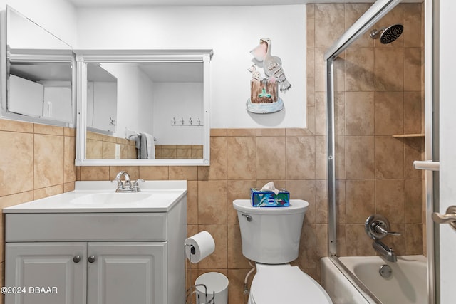 full bathroom featuring shower / bath combination with glass door, vanity, toilet, and tile walls