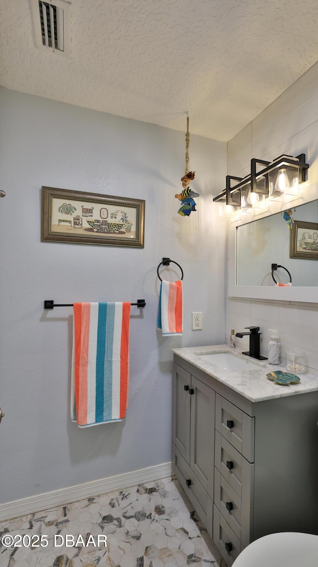 bathroom featuring visible vents, baseboards, a textured ceiling, and vanity