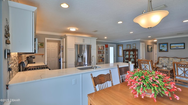 kitchen with light stone countertops, a peninsula, ornamental molding, a sink, and appliances with stainless steel finishes