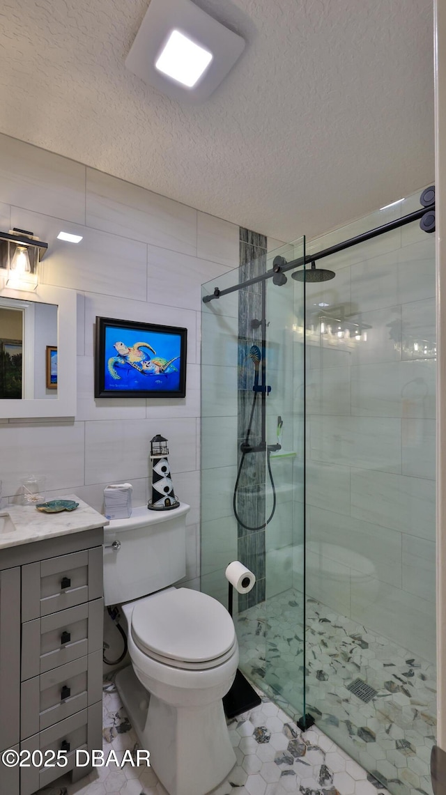 full bathroom with a stall shower, a textured ceiling, tile walls, and vanity