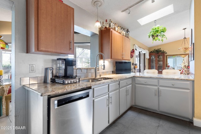kitchen featuring vaulted ceiling with skylight, stainless steel dishwasher, light tile patterned floors, a sink, and decorative light fixtures
