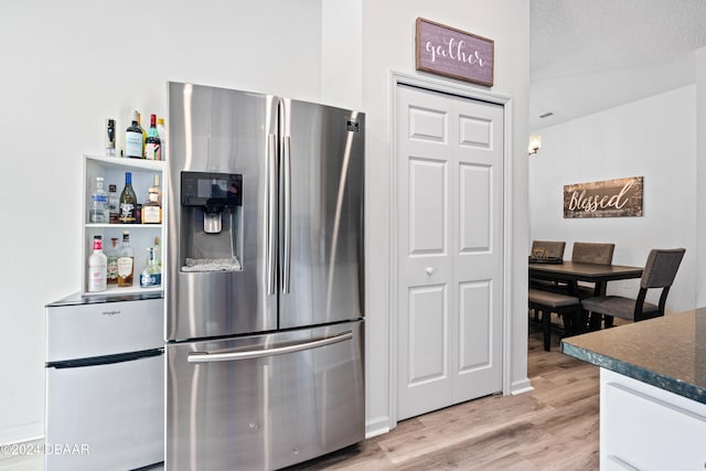 kitchen featuring stainless steel fridge with ice dispenser, a textured ceiling, light wood-type flooring, and white cabinetry