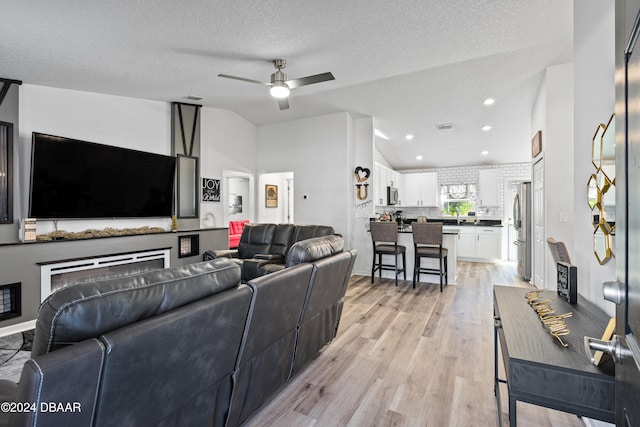 living room featuring a textured ceiling, ceiling fan, and light hardwood / wood-style flooring