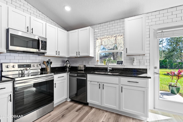 kitchen with white cabinets, appliances with stainless steel finishes, vaulted ceiling, and a textured ceiling