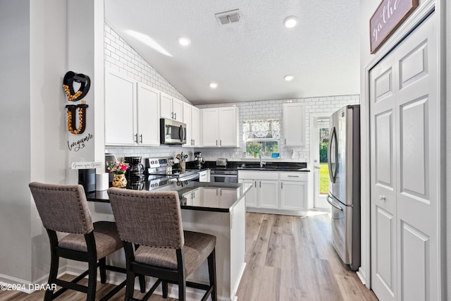 kitchen with stainless steel appliances, white cabinetry, a kitchen breakfast bar, kitchen peninsula, and lofted ceiling