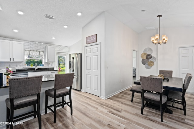 dining area with sink, a textured ceiling, high vaulted ceiling, a chandelier, and light wood-type flooring