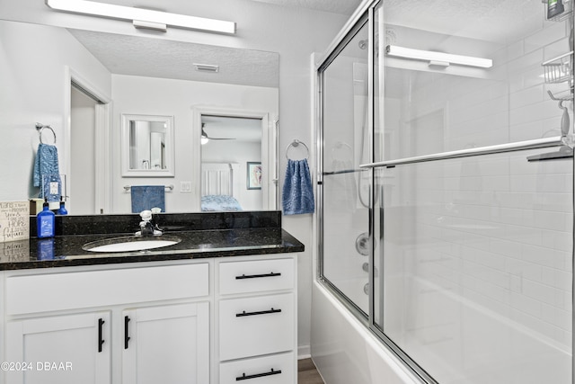 bathroom with bath / shower combo with glass door, vanity, and a textured ceiling