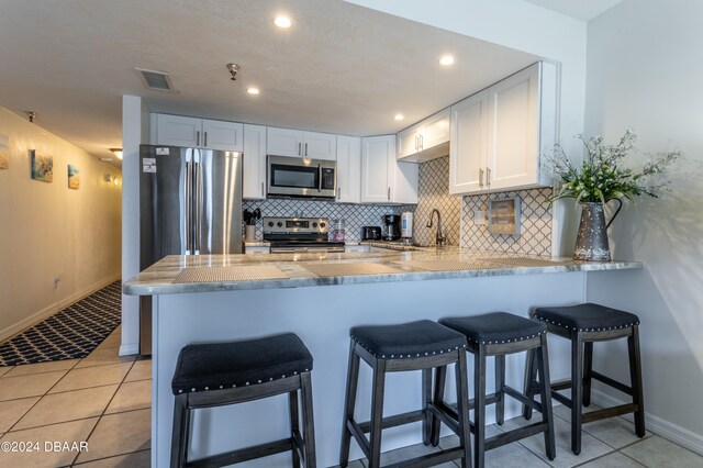 kitchen with white cabinets, a kitchen bar, appliances with stainless steel finishes, and kitchen peninsula