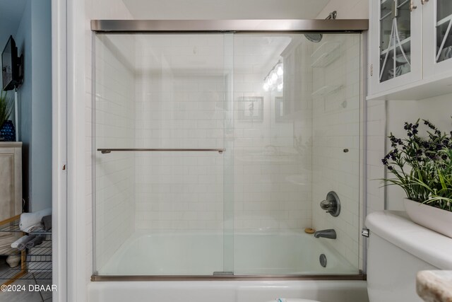 bathroom with bath / shower combo with glass door and toilet