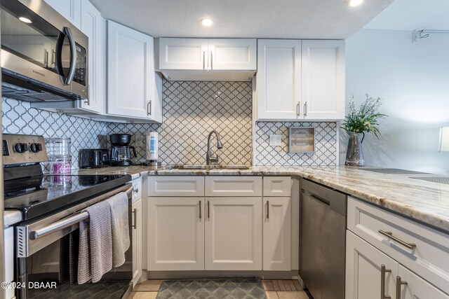 kitchen with white cabinetry, appliances with stainless steel finishes, sink, and light stone countertops