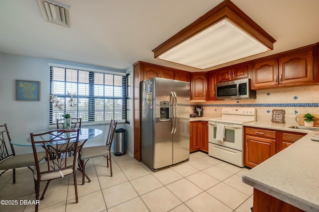 kitchen featuring light tile patterned floors, brown cabinetry, backsplash, and stainless steel appliances