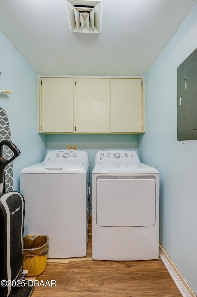 washroom featuring light wood-type flooring, electric panel, cabinet space, baseboards, and washing machine and clothes dryer