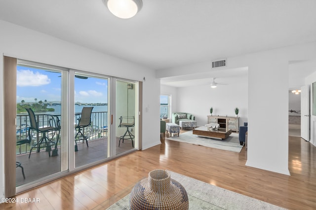 living room with ceiling fan, a water view, and wood-type flooring