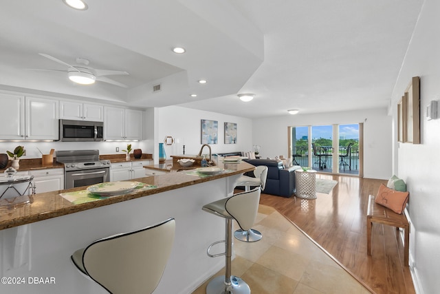 kitchen with stainless steel appliances, sink, light hardwood / wood-style flooring, dark stone countertops, and white cabinets