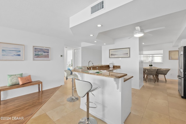 kitchen with kitchen peninsula, a kitchen breakfast bar, stainless steel fridge, ceiling fan, and light tile patterned flooring