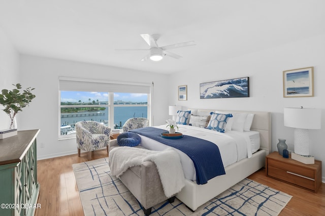 bedroom with ceiling fan, a water view, and wood-type flooring