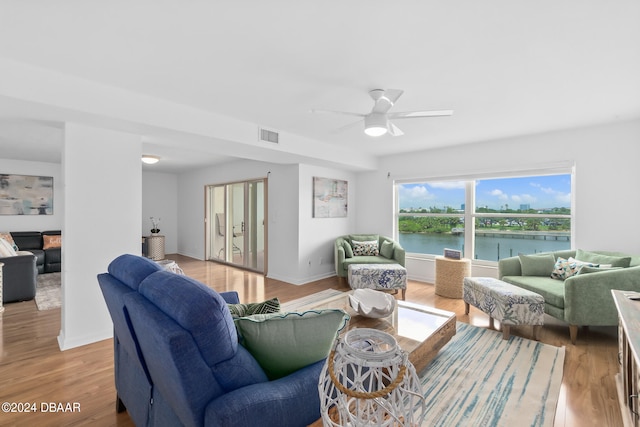 living room with ceiling fan, a water view, and light wood-type flooring