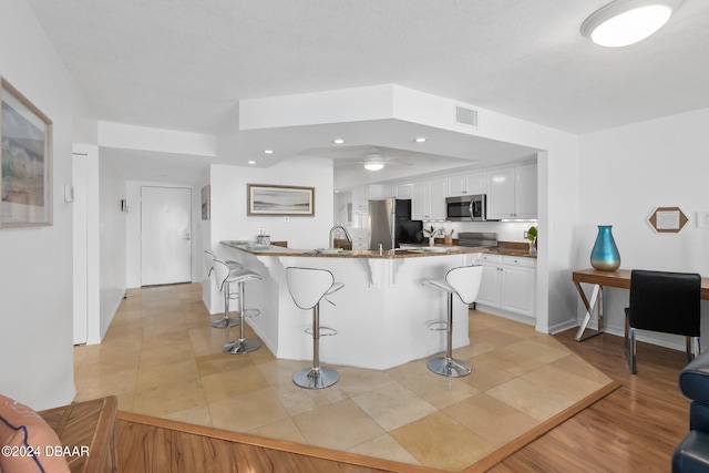 kitchen with white cabinets, light wood-type flooring, a breakfast bar, and stainless steel appliances