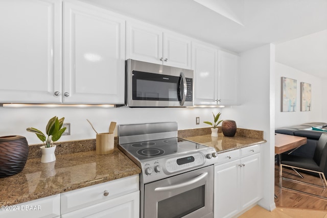 kitchen featuring stainless steel appliances, white cabinetry, and dark stone counters