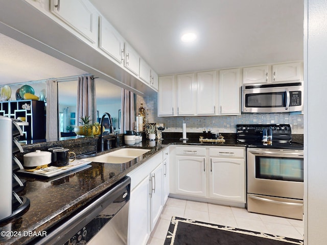 kitchen with dark stone counters, white cabinets, sink, light tile patterned floors, and appliances with stainless steel finishes