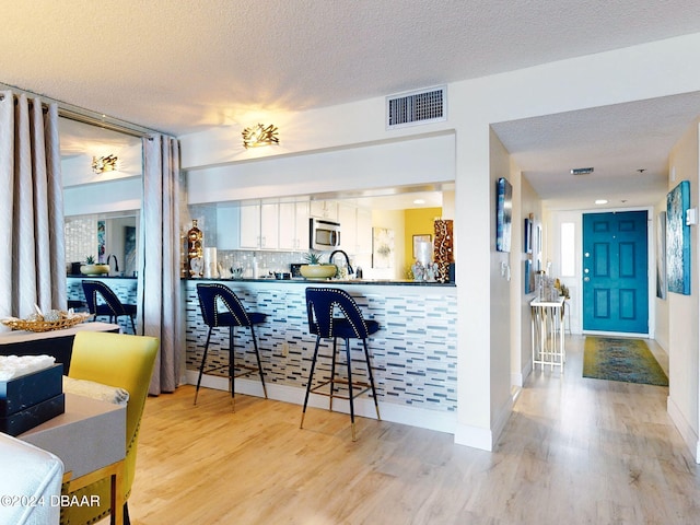 kitchen with backsplash, white cabinetry, light hardwood / wood-style floors, and a textured ceiling