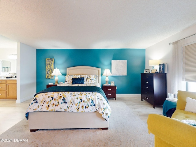 bedroom featuring a textured ceiling, connected bathroom, and light hardwood / wood-style flooring