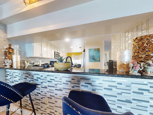 kitchen featuring white cabinets, decorative backsplash, appliances with stainless steel finishes, and dark stone counters