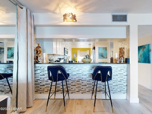 bar featuring white cabinets, light hardwood / wood-style flooring, refrigerator, and a textured ceiling