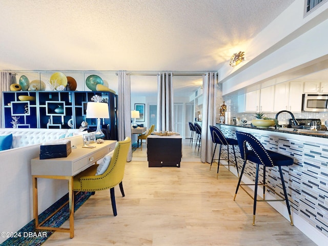 kitchen featuring backsplash, light hardwood / wood-style flooring, white cabinets, and a textured ceiling