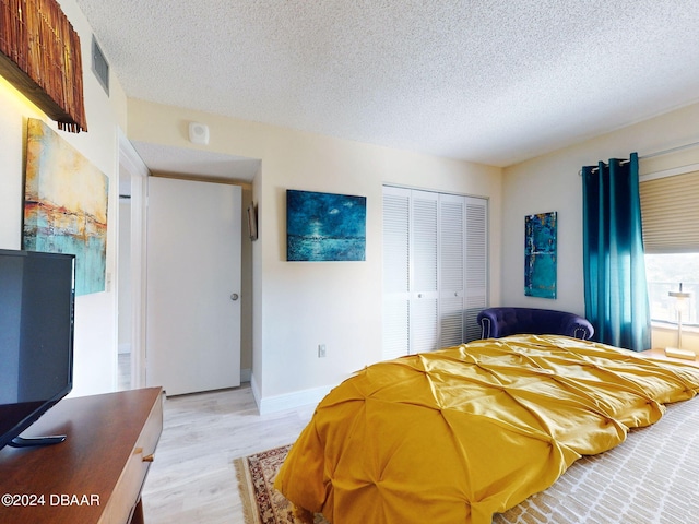 bedroom with a textured ceiling, light hardwood / wood-style floors, and a closet