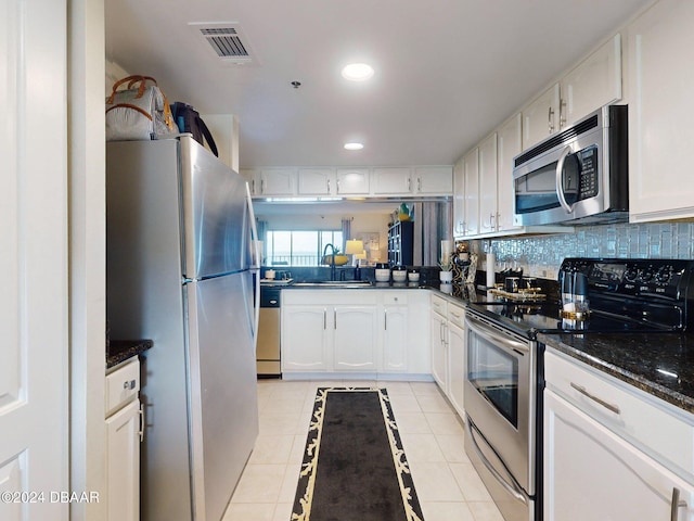 kitchen featuring appliances with stainless steel finishes, sink, dark stone countertops, white cabinets, and light tile patterned flooring