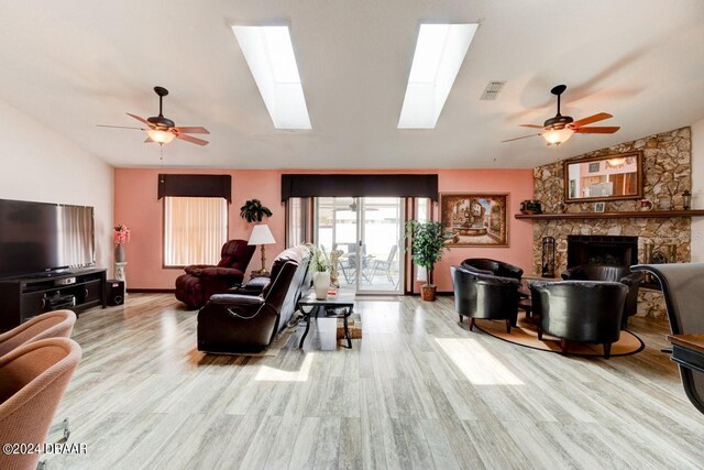 living room featuring a fireplace, light hardwood / wood-style floors, ceiling fan, and lofted ceiling with skylight