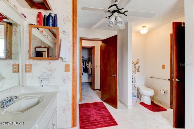 bathroom with toilet, tile patterned flooring, a textured ceiling, vanity, and ceiling fan