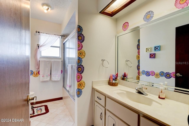 bathroom featuring tile patterned flooring, enclosed tub / shower combo, a textured ceiling, a skylight, and vanity