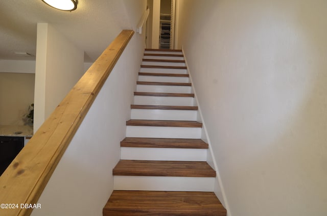 staircase with wood-type flooring and a textured ceiling