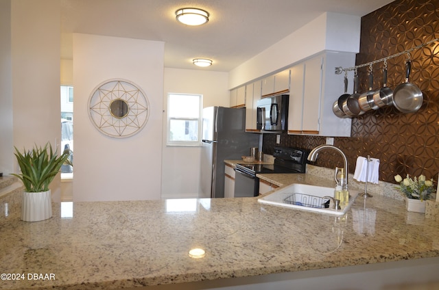 kitchen with sink, black appliances, kitchen peninsula, tasteful backsplash, and light stone countertops