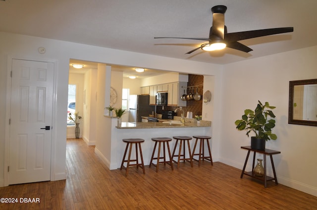 kitchen featuring black appliances, wood-type flooring, backsplash, kitchen peninsula, and ceiling fan