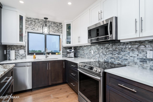 kitchen featuring dark brown cabinetry, white cabinets, decorative light fixtures, and appliances with stainless steel finishes