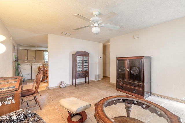 living area featuring ceiling fan, washer and clothes dryer, light tile patterned floors, and a textured ceiling