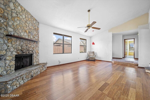 unfurnished living room with baseboards, a ceiling fan, lofted ceiling, wood finished floors, and a stone fireplace