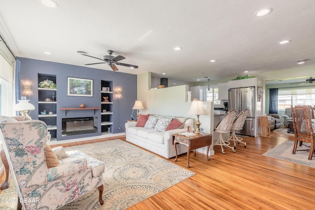 living room with a textured ceiling, light hardwood / wood-style flooring, and ceiling fan