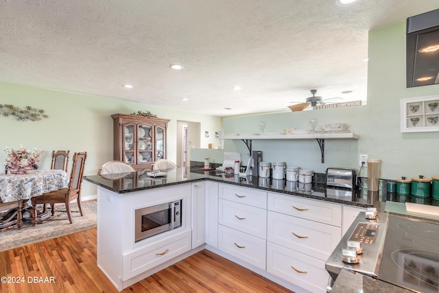 kitchen featuring stainless steel microwave, white cabinetry, kitchen peninsula, and light hardwood / wood-style flooring