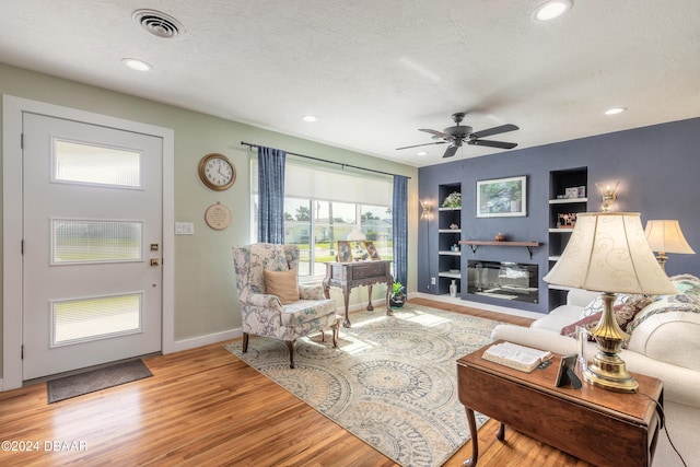 living room featuring a textured ceiling, light hardwood / wood-style flooring, ceiling fan, and built in features