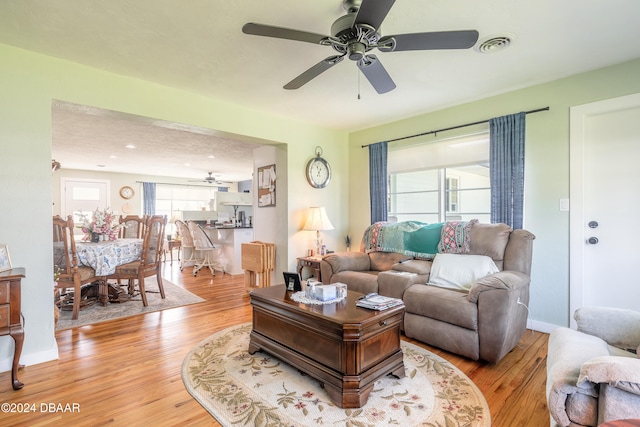 living room featuring ceiling fan, a textured ceiling, and light wood-type flooring