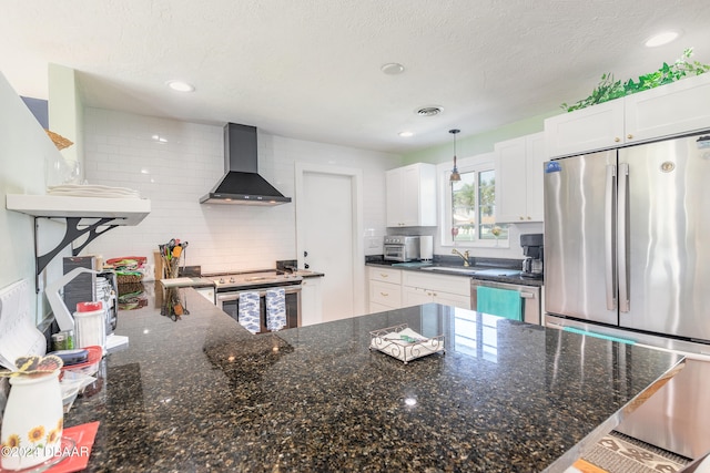 kitchen with white cabinets, hanging light fixtures, a textured ceiling, wall chimney range hood, and appliances with stainless steel finishes