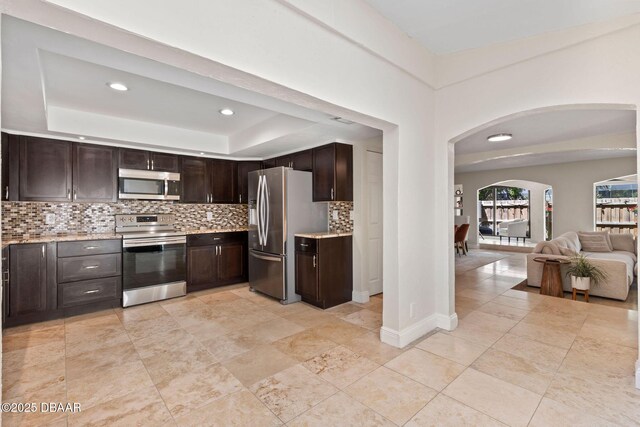 208 Pine Cone Trl, Ormond Beach, FL 32174 - kitchen with stainless steel appliances, a tray ceiling, arched walkways, decorative backsplash, and dark brown cabinets