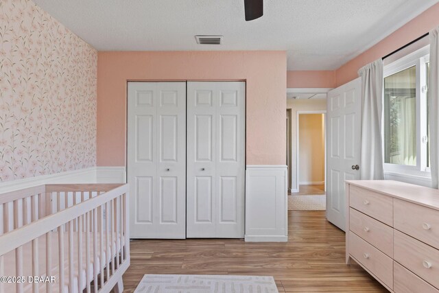 208 Pine Cone Trl, Ormond Beach, FL 32174 - bedroom featuring wallpapered walls, light wood-type flooring, a textured ceiling, a closet, and wainscoting