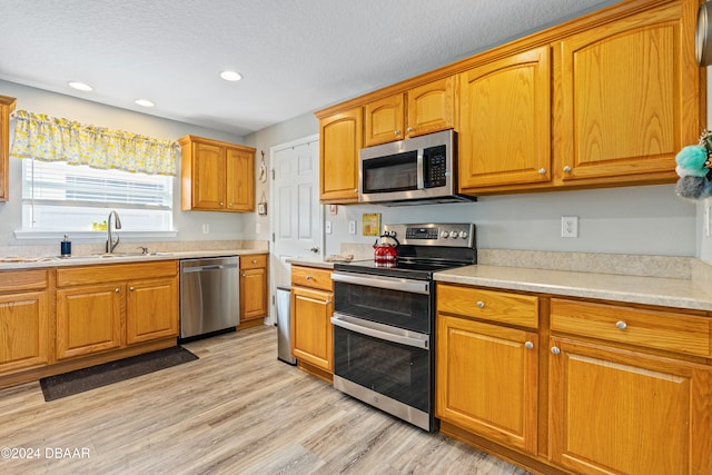 kitchen with appliances with stainless steel finishes, a textured ceiling, light hardwood / wood-style flooring, and sink