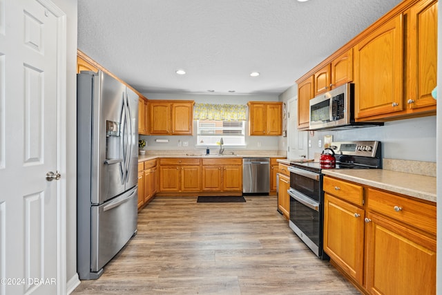 kitchen with a textured ceiling, light wood-type flooring, stainless steel appliances, and sink