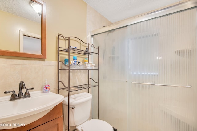 bathroom featuring a textured ceiling, an enclosed shower, toilet, vanity, and tile walls